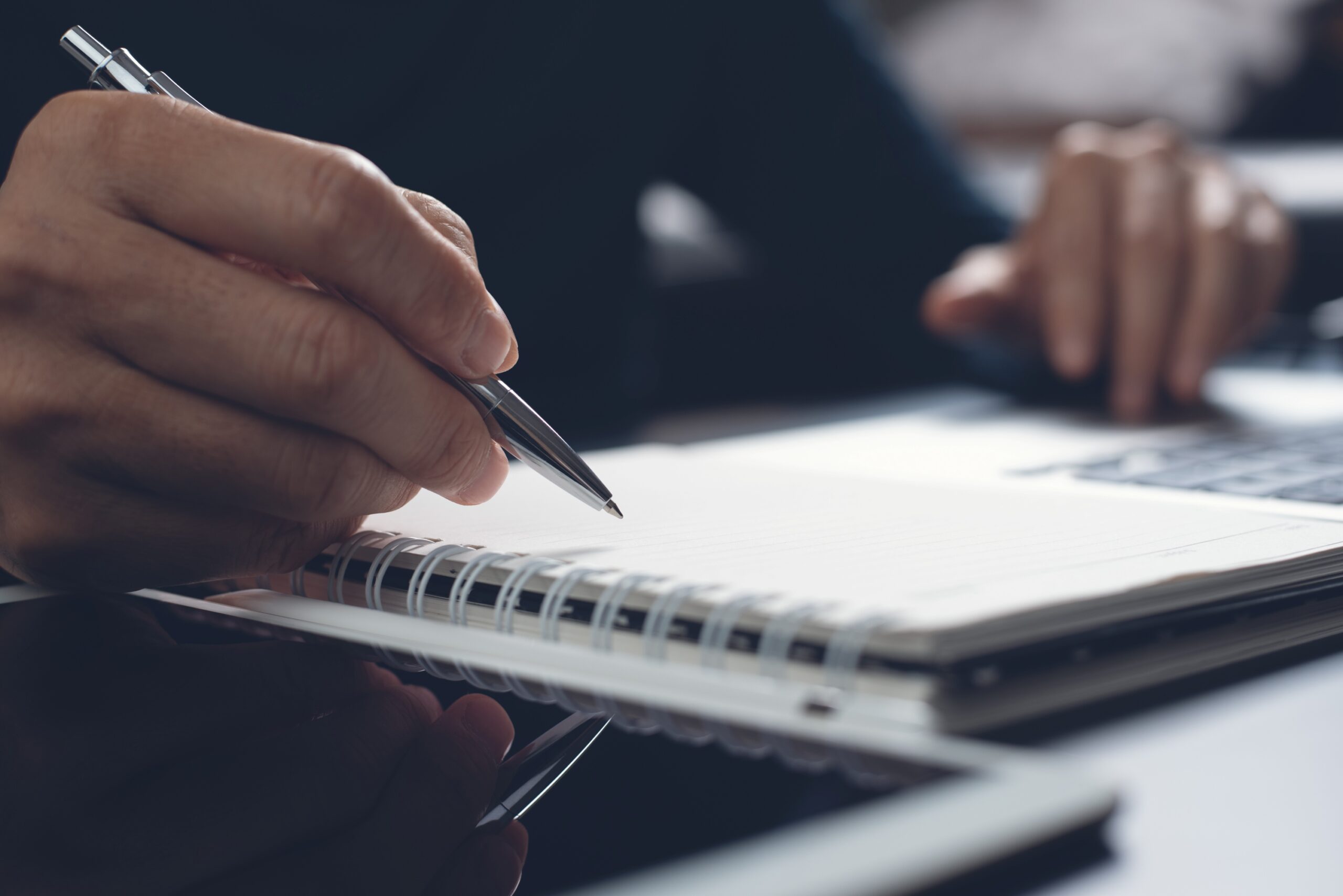 hand holding a pen over top of a notebook and ipad