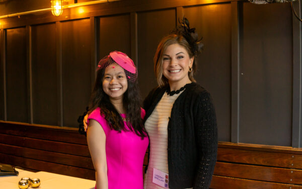 Two women pose in dresses and fascinators