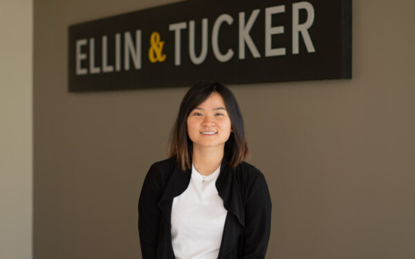 Nu Do tax manager standing in front of Ellin & Tucker sign against a taupe colored wall