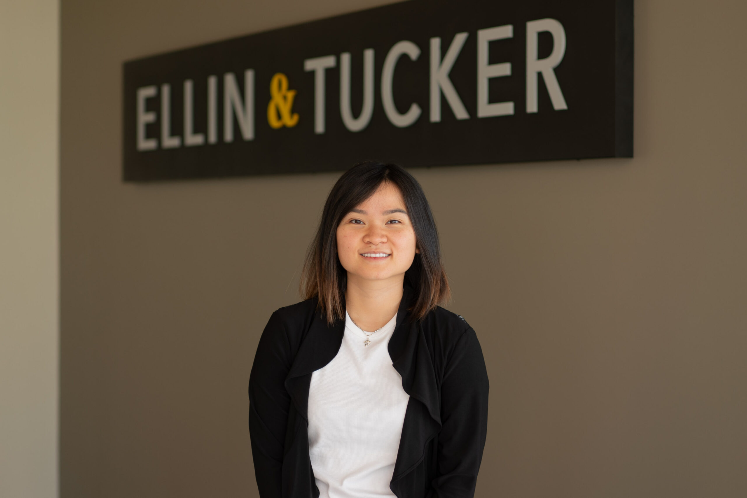 Nu Do tax manager standing in front of Ellin & Tucker sign against a taupe colored wall