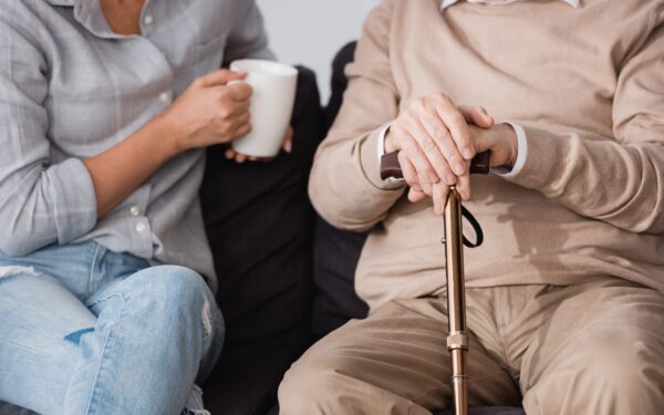 woman with cup of tea near aged father holding cane sitting on couch