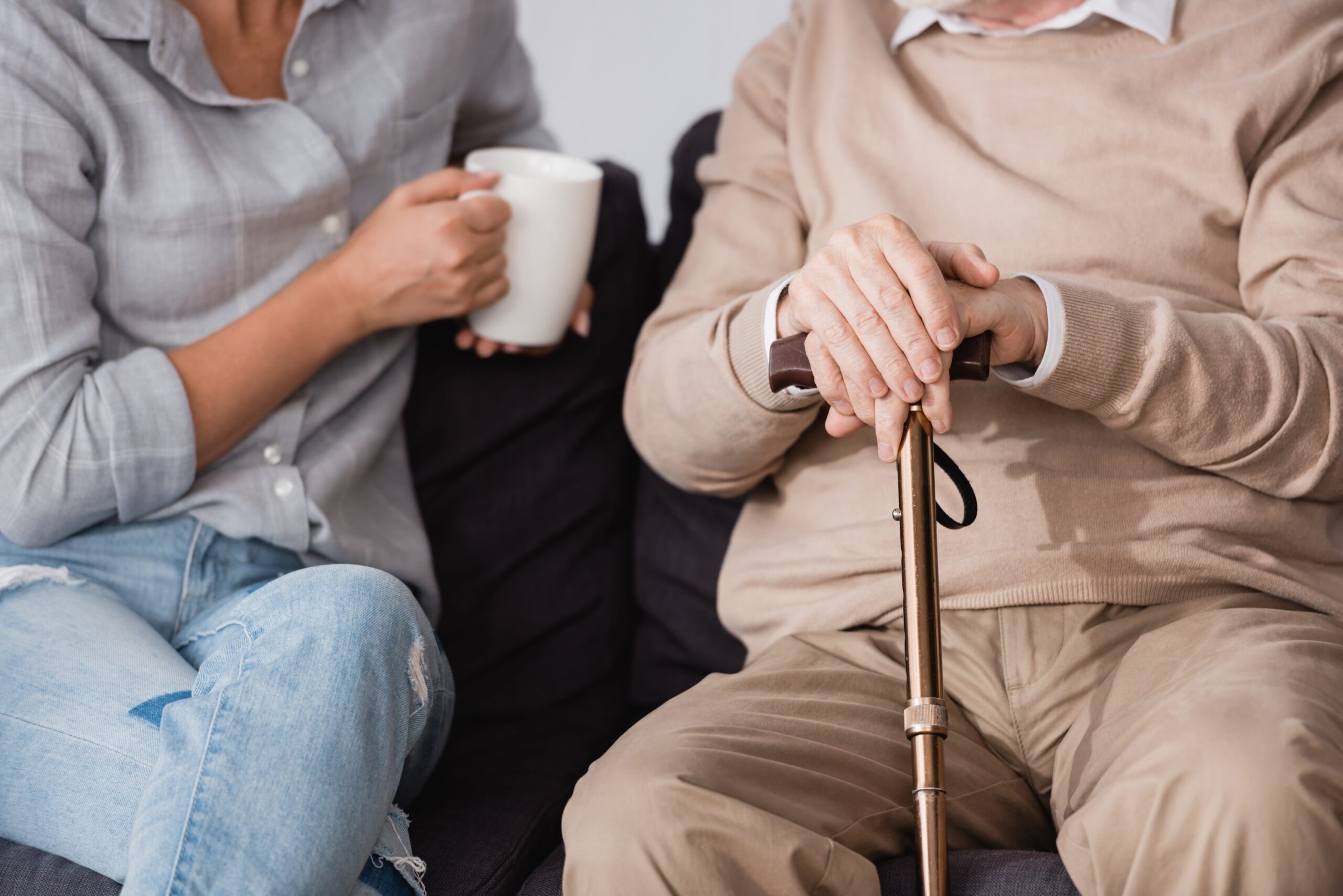 woman with cup of tea near aged father holding cane sitting on couch