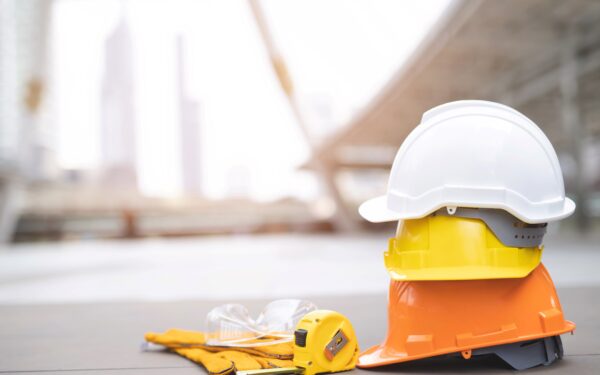 white, yellow, and orange hard hats stacked on top of one another on concrete floor