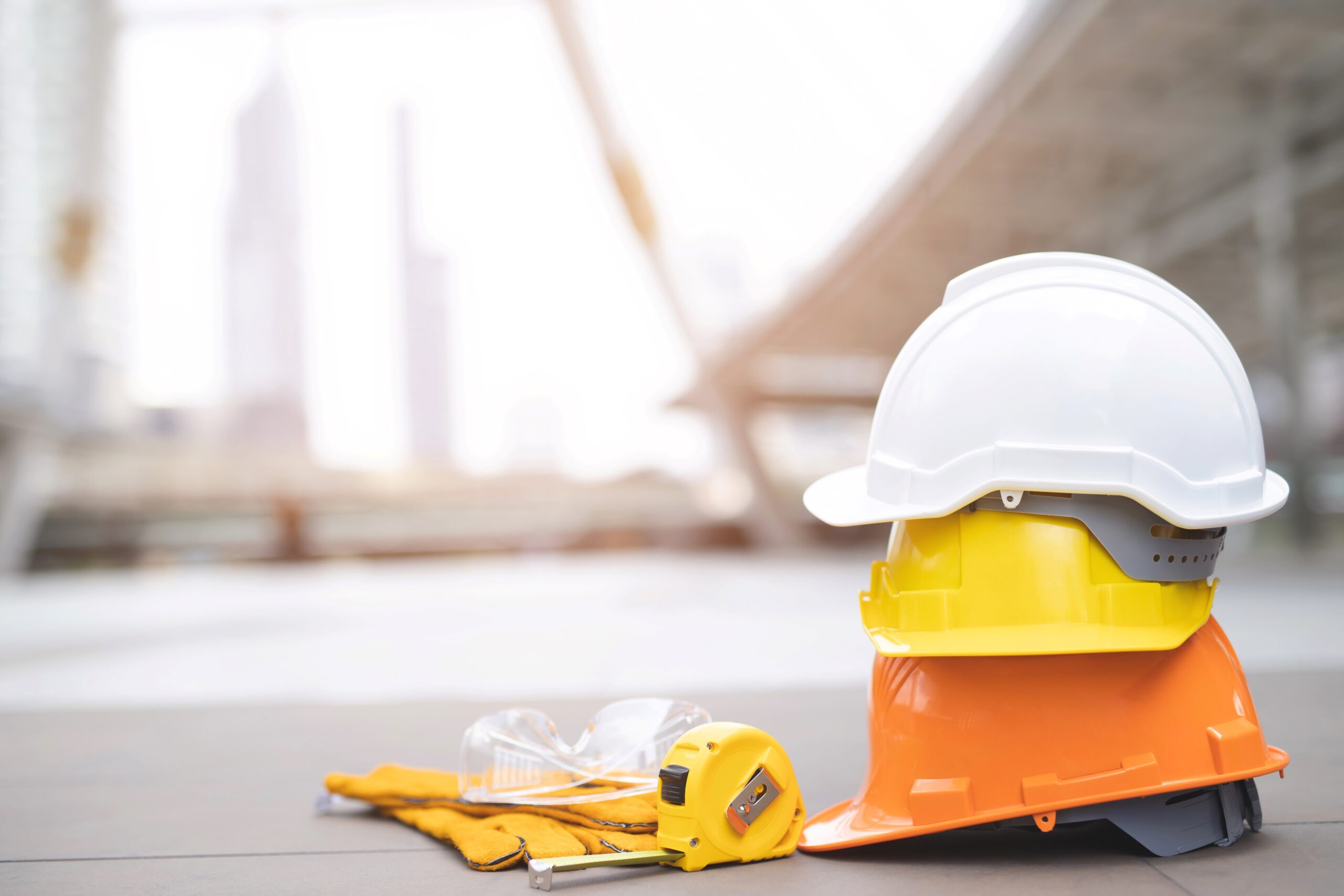 white, yellow, and orange hard hats stacked on top of one another on concrete floor