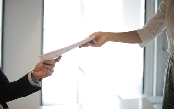 woman handing man documents in front of a window