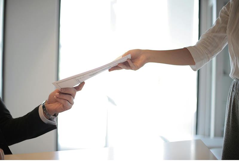 woman handing man documents in front of a window